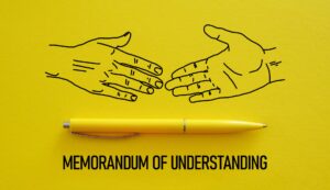Two hands getting ready to shake a yellow pen and under it says Memorandum of Understanding