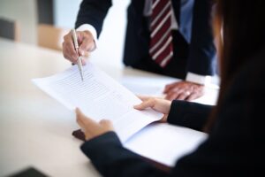Two sets of hands one holding documents and one holding a pen going over documents