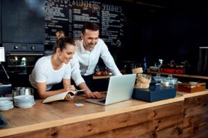 Two people standing at a counter looking at a laptop and going over paperwork